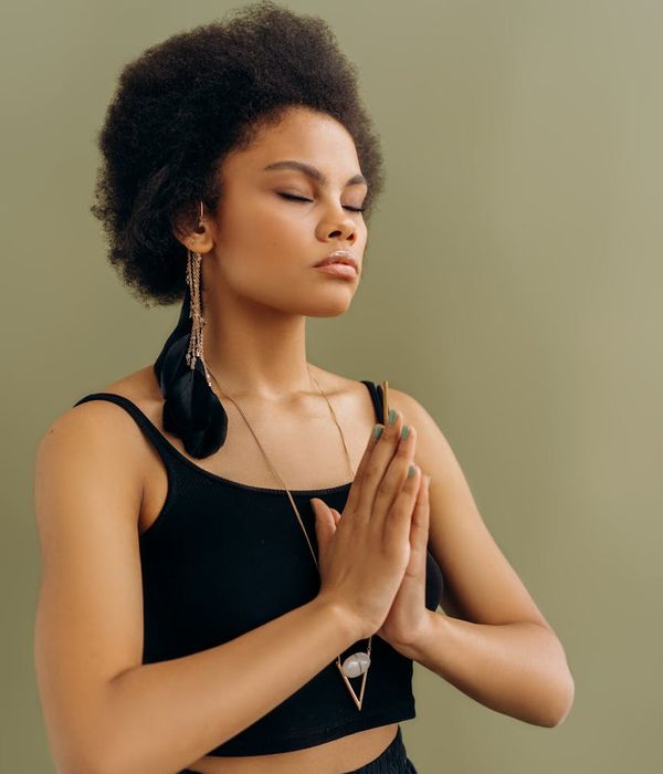 Woman in a peaceful yoga pose against a solid purple background, embodying calm focus.